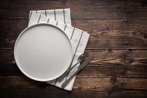 Top view of empty ceramic white plate, fork and table knife on wooden table Stock Photos