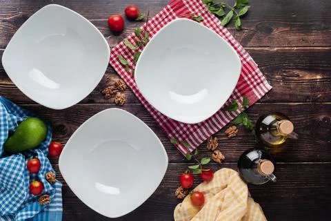 Top view of empty dinner plates with vegetables around them on wooden table Stock Photos