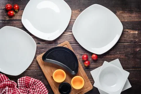 Top view of empty dinner plates with vegetables around them on wooden table Stock Photos