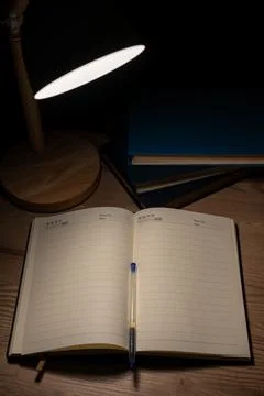 Top view of an empty lined notebook with a pen on a wooden table illuminated. Stock Photos