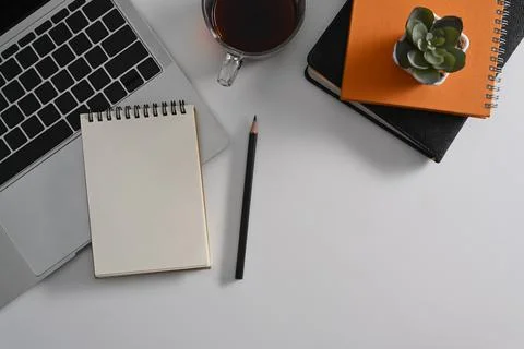 Top view empty notepad, laptop computer and coffee cup on white table. Flat lay. Stock Photos