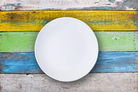 Top view of empty white plate put on colorful wood table with space for copy. Stock-Fotos