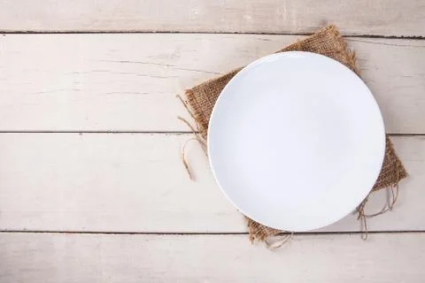 Top view of empty white plate put on sack and white wood table with space for Stock Photos