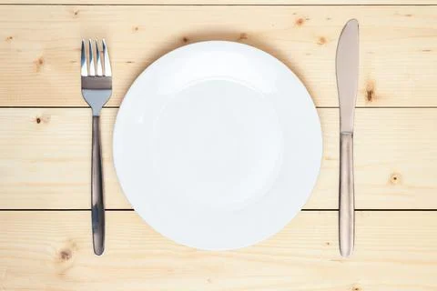Top view of an empty white plate, fork and table knife on a wooden background Stock Photos