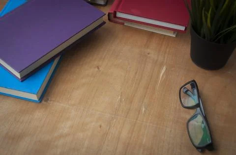 Top view of empty wooden table surrounded by books, glasses and plant. Stock Photos