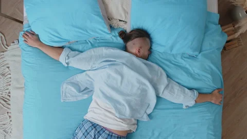 Top view exhausted tired caucasian young guy in pajamas jumping and falling flat Stock Footage 166300534