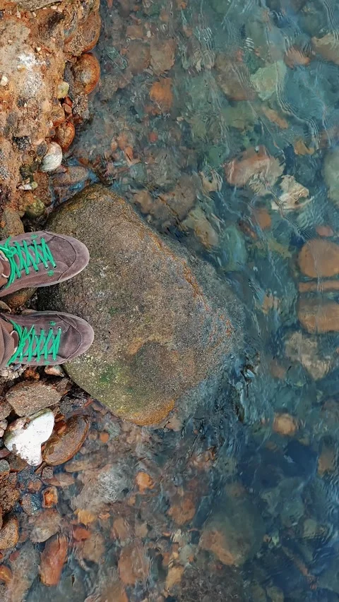 Top view of feet on a rock at the edge of clear winter water in Italy Stock Footage 330752138