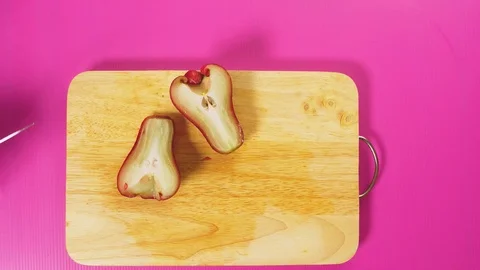 Top view, female hand cuts a fruit with a knife on a wooden board, rose apple Stock Footage 100411017