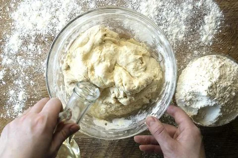 Top view of female hands adding oil to dough on flour background, bread baking Stock Photos