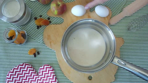Top view female hands break egg into a metal pan with milk on cutting board in Stock Footage 137828346