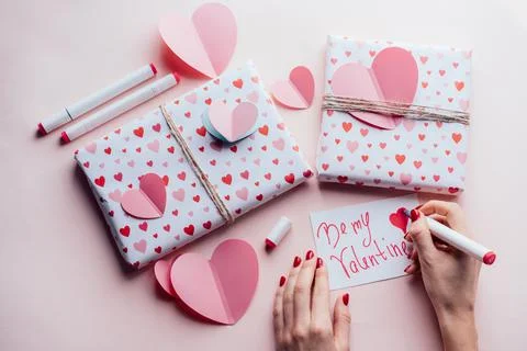 Top view of female hands on pink background with gifts writing valentine card BE Stock Photos