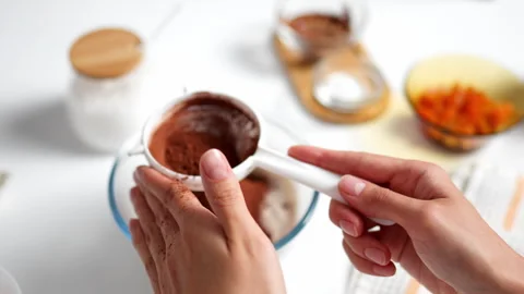 Top view of female hands sifting cocoa powder through sieve into bowl with f 動画素材 247367565