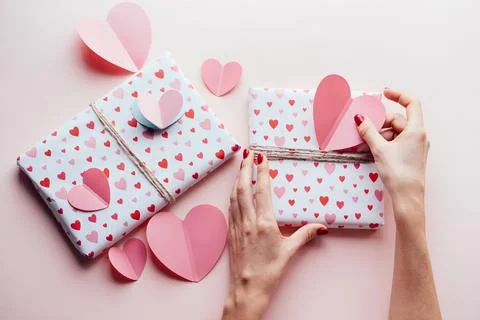 Top view of female hands wrapping valentine's gifts and decorating them with big Stock Photos