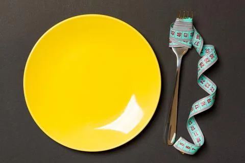 Top view of fork with measure tape near round plate on black background. We.. Stock Photos