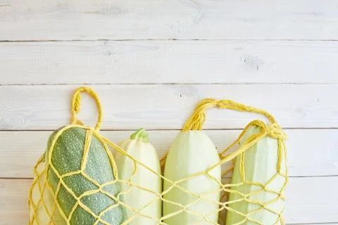 Top view of fresh courgettes in row bag over white rustic background. Stock Photos