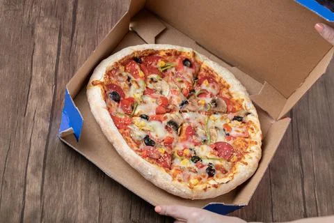 Top view of fresh mixed pizza in pizza box over wooden background Stock Photos