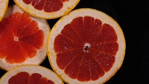 Top view of fresh red grape-fruit slices on black dish, rotating clockwise Stock Footage 74695030