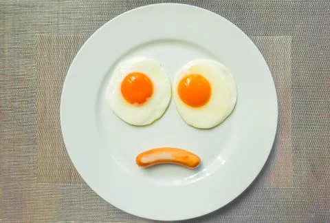 Top view of fried egg and sausage is sad face on white plate  on table. Stock Photos