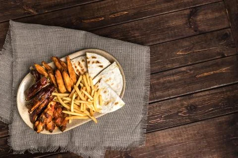 Top view on fried pork ribs, french fries and pita bread on plate. Rustic foo 库存照片