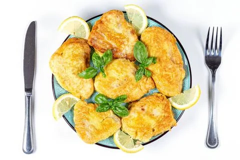 Top view, fried tilapia in batter on a plate with basil leaves and lemon slic Фото
