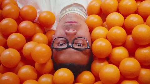 Top view of funny man with glasses lying in orange balls Stock Footage 272320833