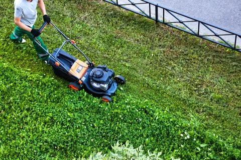 Top view of gardener in uniform using lawnmower mowing lawn in garden Stock Photos