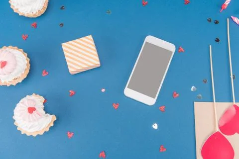 Top view of gift box, smartphone and cakes isolated on blue, birthday party Foto stock