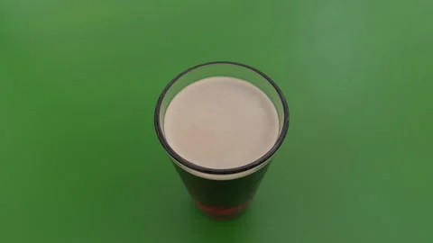 Top view of glass filled with dark beer and creamy foam on bright green Stock Footage 338133981