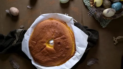 Top View of Golden Sponge Cake on Parchment Paper with Easter Eggs and Feathers Stock Footage 332229195