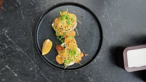Top view of a gourmet dish with poached eggs, sauce, and fresh herbs on a black Stock Footage 320226693