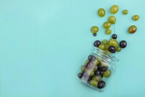 Top view of grape berries spilling out of jar on blue background with copy .. Stock Photos