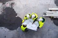 A Top View Of Group Of Engineers With Blueprints Standing On Construction Site. Stock Photos