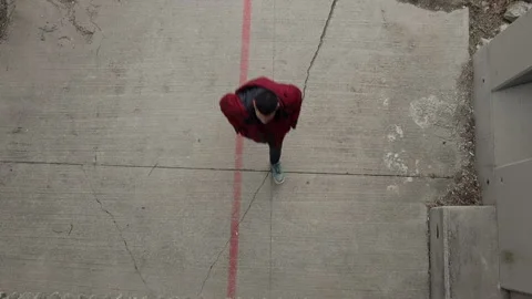 Top View of A guy in a red coat walking on a concrete sidewalk Stock Footage 142491123