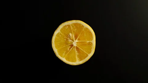 TOP VIEW: Half of lemon rotates on a black surface - Stop motion Видео 100258235