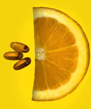 Top view of half orange slice and vitamins on yellow background. Stock Photos