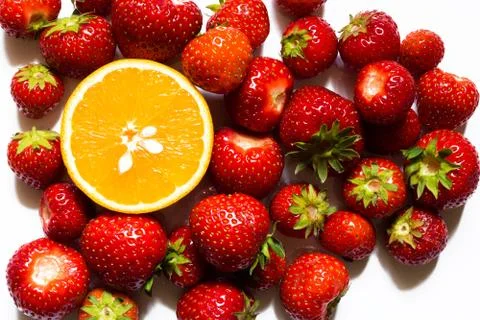 Top view of half of orange surrounded by red strawberries on white background Stock Photos