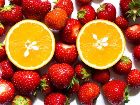 Top view of half of orange surrounded by red strawberries on white background Stock Photos