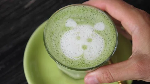 Top view of a hand grabbing matcha ice tea with latte art of a bear on it Stock Footage 150435014