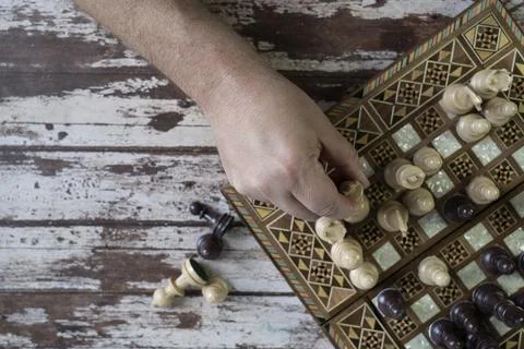 Top view of a hand playing chess game on old peeled of colored wooden table Stock Photos