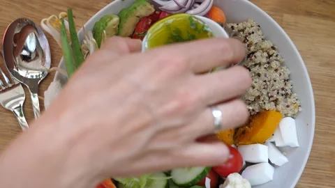 Top view of hand pouring dressing onto warm salad with soba noodles, quinoa and Stock Footage 140010010