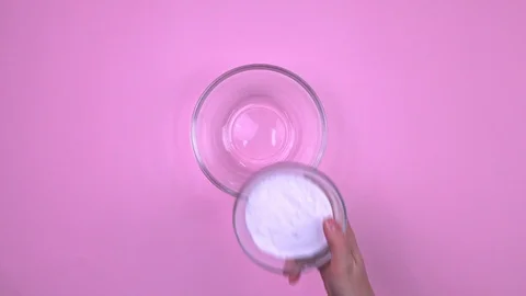 Top view of a hand pouring white powder into a glass bowl and adds the yellow Stock-Footage 126531431
