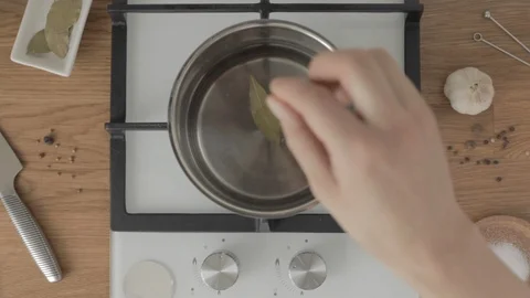 Top view hand puts bay leaf in metal pan with water on stove Vídeo Stock 113751021