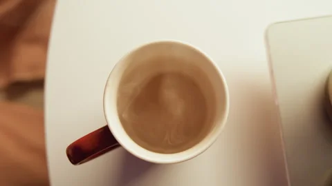 Top view hand reaching for steaming coffee mug on round white table in cozy Stock Footage 345655749