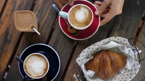 Top view of hand serving a cup of cappuccino on a wooden table next to another Stock Footage 146048283