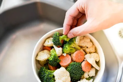 Top view of hand taking chopped vegetables from a bowl full of broccoli, caulifl Stock Photos