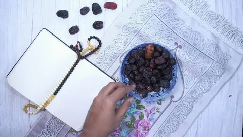 Top view of hand taking date from bowl placed on prayer mat with notebook a.. Stock Footage 333031486