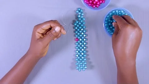 Top view of a hand threading beads. Weaving and pattern arrangements Stock Footage 201316564