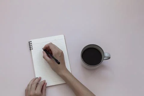 Top view of hand writing on notebook near cup of black coffee on pink background Stock Photos
