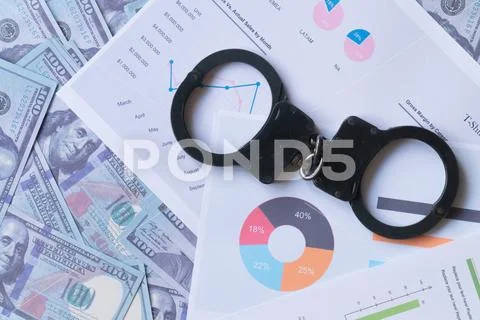 Top view handcuffs against the background of charts and hundred-dollar bills Stock Photos