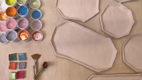 Top view of handmade clay plates and glaze jars ready for painting Stock Footage 306278315